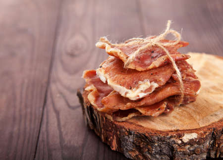 Pieces of jerky in a pile tied with twine lie on a cut of a tree on a wooden background. Copy spaes.の写真素材