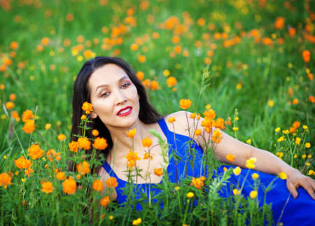 A beautiful Altai girl in a blue dress lies among the flowers in the Altai mountains in summer. Tourism concept.の写真素材