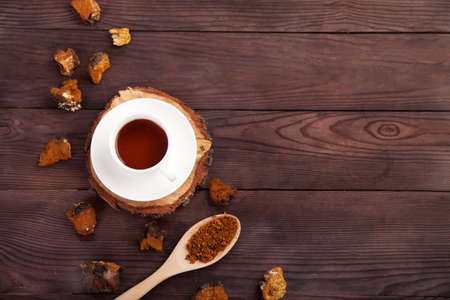Chaga mushroom coffee drink in a white cup on a wooden stand, scattered pieces of chaga and a spoon with chaga powder on a wooden background. copy space.の写真素材