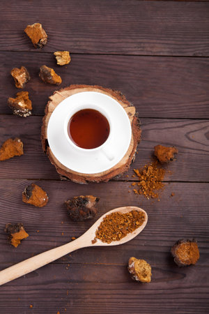 Chaga mushroom coffee drink in a white cup on a wooden stand, scattered pieces of chaga and a spoon with chaga powder on a wooden background. vertical, top view.の写真素材