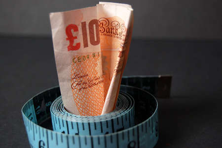 This is an image of a ten pound note and measuring tape, with a stack of pennies in the background.の写真素材