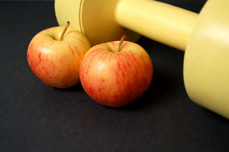 This is an image of a two apples and a yellow dumbbell.の写真素材
