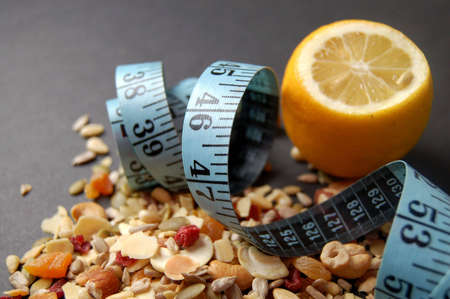 This is an image of a lemon, measuring tape and some country mix fruit/cereal.の写真素材