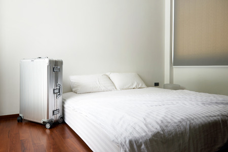 Opened door to modern white and clean bedroom interior with aluminium suit caseの写真素材