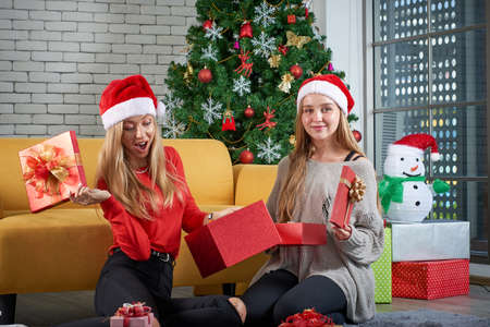 Merry christmas and Happy new year holiday, Beautiful white caucasian female celebrate, exchanging gifts relax in front of a yellow sofa and christmas tree in roomの写真素材