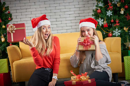 Merry christmas and Happy new year holiday, Beautiful white caucasian female celebrate, exchanging gifts relax in front of a yellow sofa and christmas tree in roomの写真素材