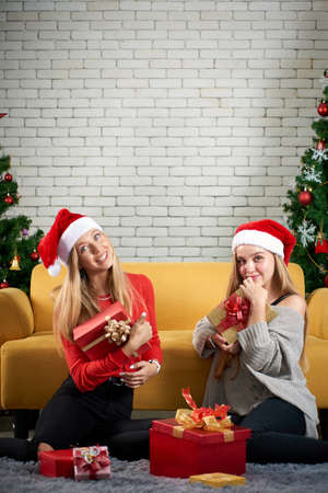 Merry christmas and Happy new year holiday, Two woman white caucasian celebrate, exchanging gifts relax in front of a yellow sofa and christmas tree.の写真素材