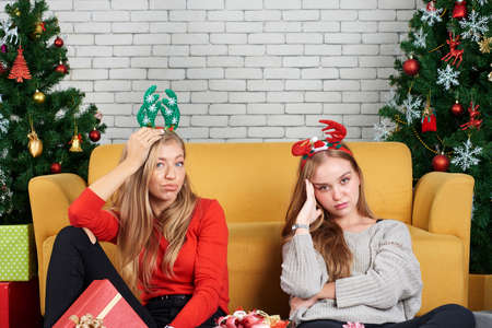 Two white young female are friend depression, tired, drunk and hangover in the morning after Christmas and New year party in room with sofa and christmas tree.の写真素材