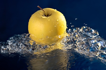 Golden apple on a blue background and splashes of waterの写真素材