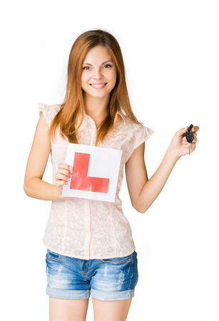 Young teenage learner driver holding L-plate and car keys, proud of passing her driving test at school.の写真素材