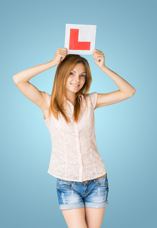 Young happy learner driver holding L-plate, proud of passing her driving test at school.の写真素材