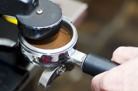 Barista with tamper and piston/portafilter in front of a grinder making espresso.の写真素材