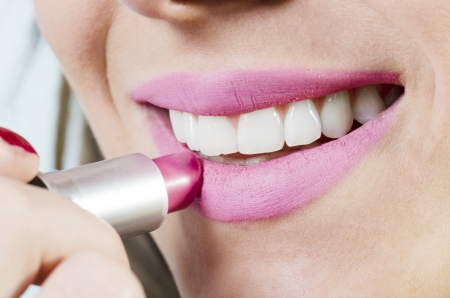 Close up of a beautiful female applying pink lipstick, white .の写真素材