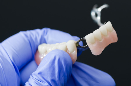 Gloved dentist hand, holding dental prosthesis on black background