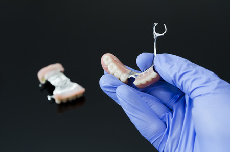 Gloved dentist hand, holding dental prosthesis on black backgroundの写真素材