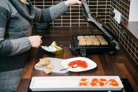 Preparation of red caviar in domestic kitchen, shallow depth of field, focus on the toast bread on the toasterの写真素材