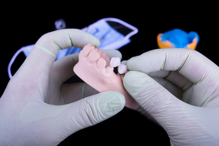 Gloved dentist hand, holding dental prosthesis on black background