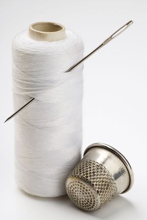 spool of thread with needle stuck in it and a thimble