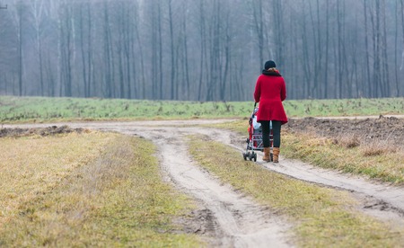 woman walking with stroller by sandy rural roadの写真素材