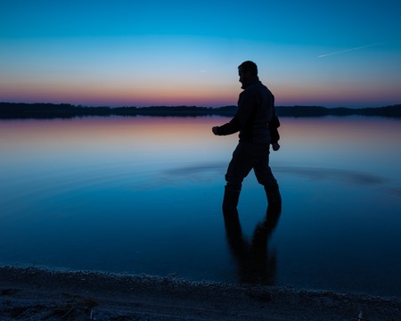 Man in lake water at sunset. Beautiful sunset with man silhouetteの写真素材