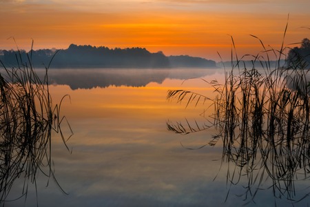 Beautiful lake sunrise with sky reflections in water. Tranquil colorful scene of typical polish lake in Mazury lake district.の写真素材