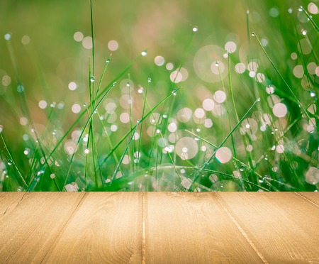 Wet springtime grass with bokeh effect and wooden floor. Abstract background with wooden planks
