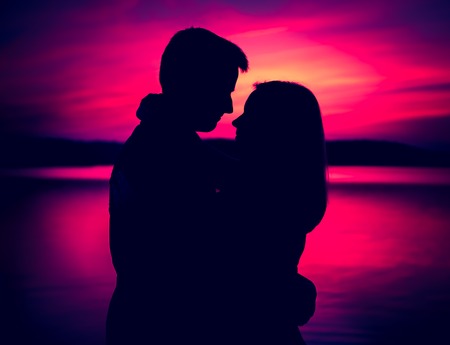 Silhouettes of hugging couple against the sunset sky. Photo with vintage mood.の写真素材