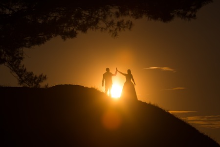 Silhouettes of wedding couple standing on hill in beautiful sunsetの写真素材