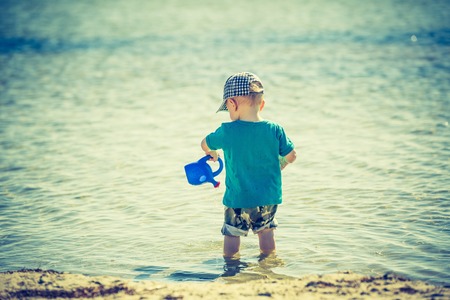 Little child playing on sea shore at good summer weather. Photo with vintage mood effect