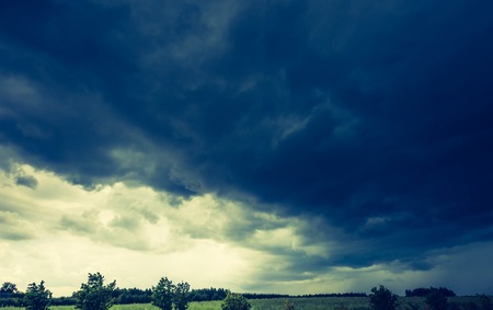 Vintage photo of dark stormy clouds over corn field at summer. Frightening storm over countryside.の写真素材