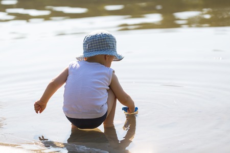 Toddler digging in coast sand with shovel. Baby playing outside on lake shore at summer.の写真素材