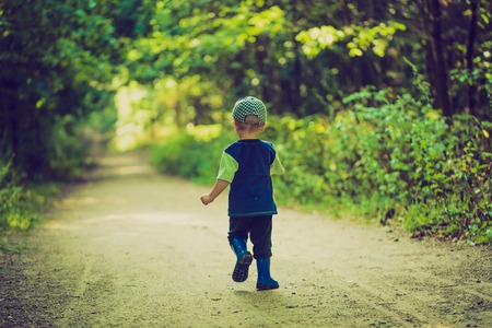 Vintage photo of little boy running and playing in forest at summerの写真素材