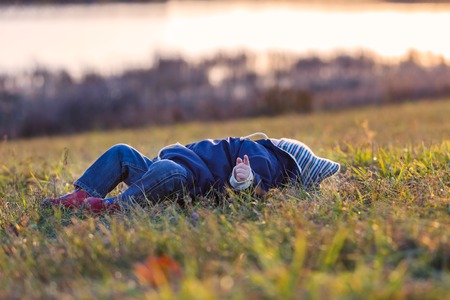 Little boy playing outdoor in autumnal landscape. Caucasian child lies on grass near lakeの写真素材