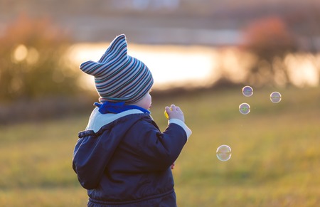 Little boy playing with soap bubbles in outdoor in autumnal landscape. Caucasian child photographed from behindの写真素材