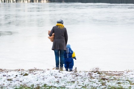 Little child (boy) playing outdoor on lake shore with his mother. Beautiful childhood in nature.の写真素材