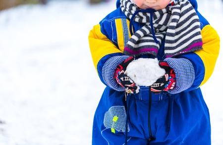 Child playing outdoor at winter with snow ball. Close up of child walking in snowy weather.