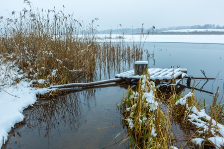 Landscape with jetty covered by snow on frozen lake shore near mouth ov river.の写真素材