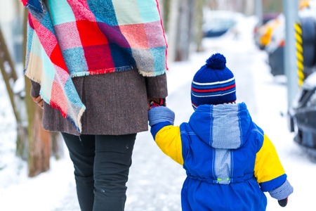 Child and mother holding their hand and walks in winter city. Close up of child walking in snowy weather.の写真素材