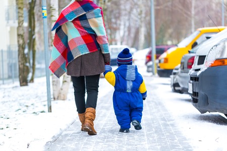 Child and mother holding their hand and walks in winter city. Close up of child walking in snowy weather.の写真素材