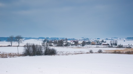 Winter field landscape under cloudy sky near small village. Polish countrysideの写真素材