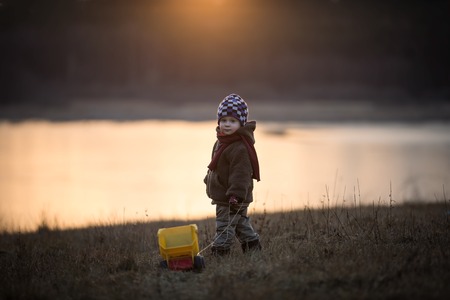 Little boy playing outdoor with a toy car. Beautiful child photo with golden light.の写真素材