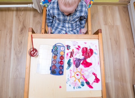 Baby boy painting with watercolors. Small caucasian child playing in home with paint and brushの写真素材