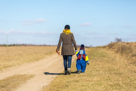 Mother and son walking by sandy rural road at springtime, photo taken from behind.の写真素材