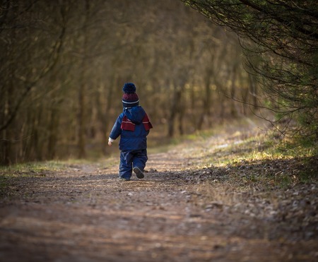 Caucasian boy playing outdoor at springtime in forest. Boy walking by forest pathの写真素材