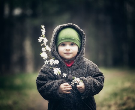 Young boy playing outdoor with cherry flowers at spring day. Vintage photo of happy caucasian boy.