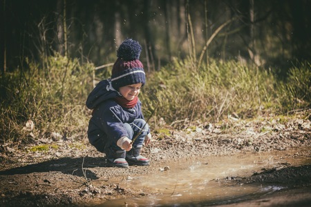 Little boy playing in puddle in spring forest. happy childhoodの写真素材