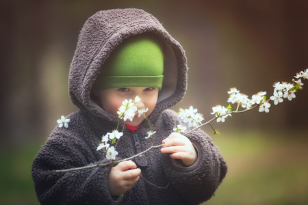 Young boy playing outdoor with cherry flowers at spring day. Vintage photo of happy caucasian boy.