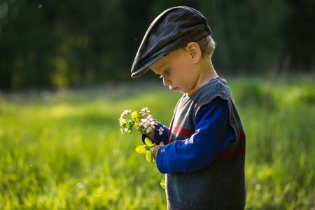 Happy caucasian boy playing outdoor at warm springtime day, boy holding blooming cherry branch