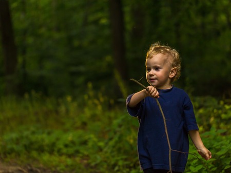 Small blonde boy playing in forest. Natural landscape with small caucasian boy.の写真素材