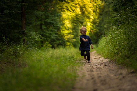 Small blonde boy playing in forest. Natural landscape with small caucasian boy.の写真素材